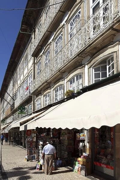 A newsagents stand under a building with a wrought iron balcony on the Largo do Toural