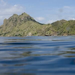 View of coastline with hills and ship from surface of sea, Mobula Point dive site, Padar Island, Komodo N. P