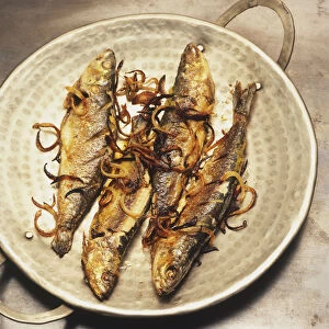 Meen porichathu, four fried sardines in silver serving dish, sprinkled with onions, overhead view