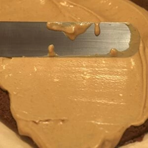 Spreading cream cake filling over layer of chocolate sponge cake