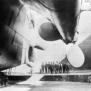 Workmen standing under one of the propellors of the Titanic, 31 May, 1911. Creator
