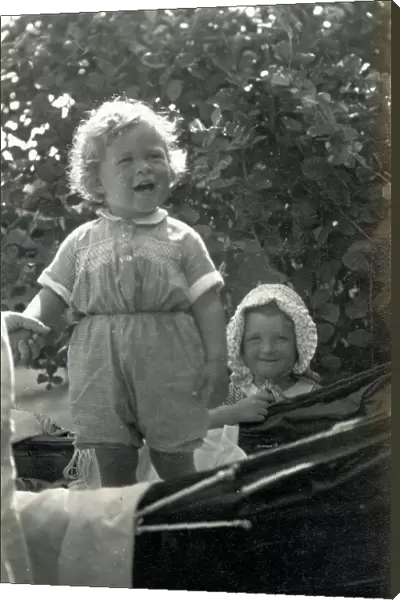 Two young siblings, one standing in a fine baby carriage