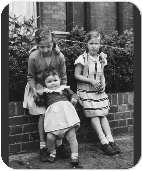 Three sisters sitting on a front garden wall