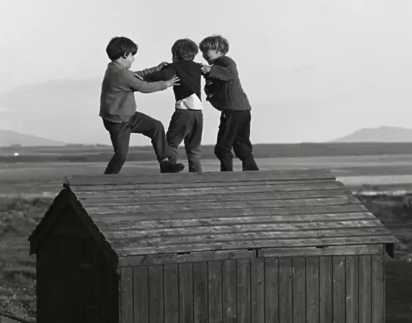 Three boys playing on top of a wooden shed