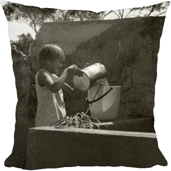 Girl pouring water from a tin into a bucket