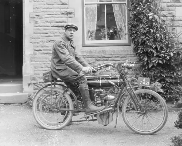Man on an early motorcycle in front of a house