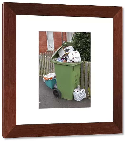 Green wheelie bin overflowing with domestic rubbish awaiting collection Cheltenham UK