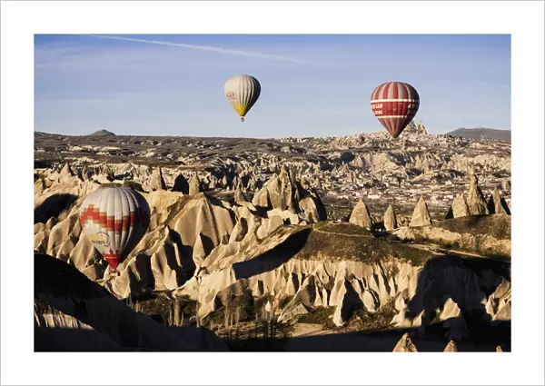 Hot air balloons flying among rock formations at sunrise in the Red Valley, Goreme National Park