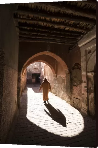 Local man dressed in traditional djellaba walking through archway in a street in the Kasbah
