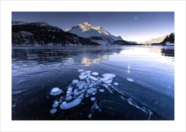 Methane bubbles in the icy surface of the lake with snowy peak illuminated by moonlight