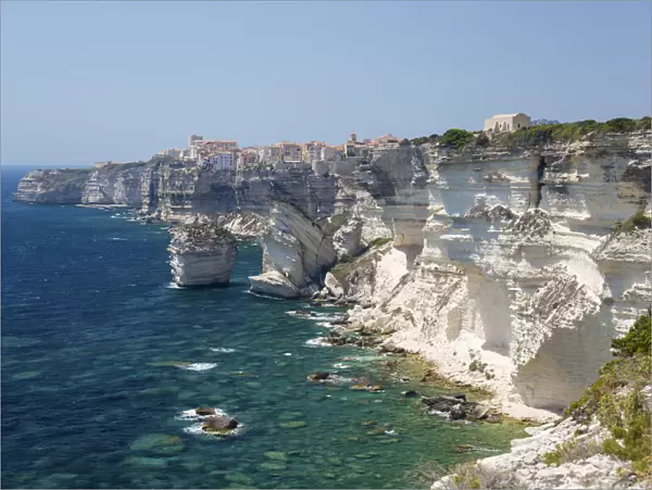 View over rocky cove along rugged limestone cliffs to the distant citadel, Bonifacio, Corse-du-Sud, Corsica, France, Mediterranean, Europe