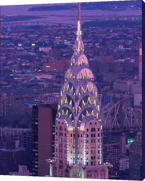 The top of the Chrysler Building illuminated in the evening with a bridge