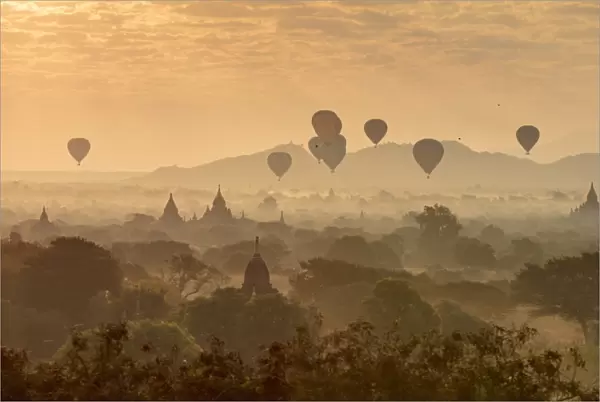 Hot air balloons fly over the temples of Bagan at sunrise on a misty morning, Myanmar