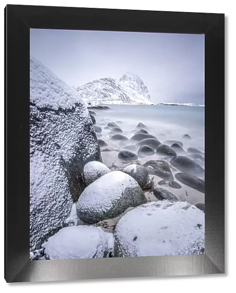 Snow covered rocks on the beach modeled by the wind surround the icy sea Pollen Vareid