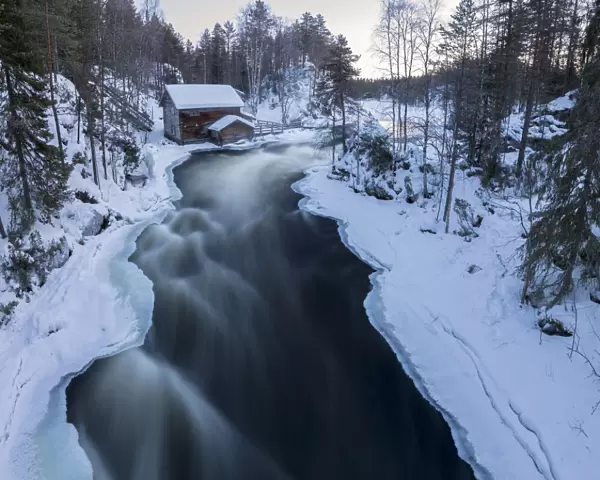 A wooden hut surrounded by the river rapids and snowy woods at dusk Juuma Myllykoski