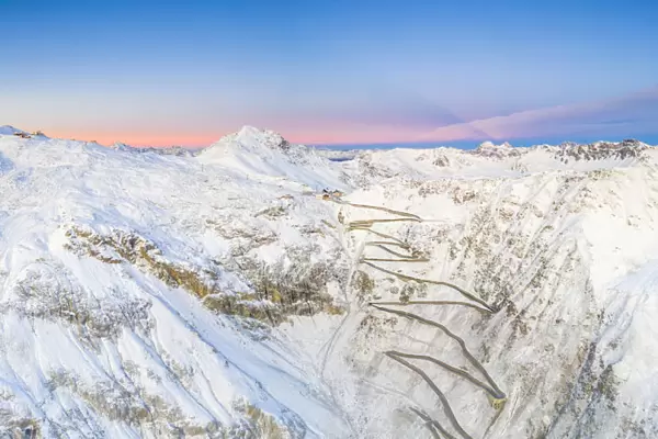 Aerial panoramic of Stelvio Pass and winding road covered with snow at dawn, Bormio