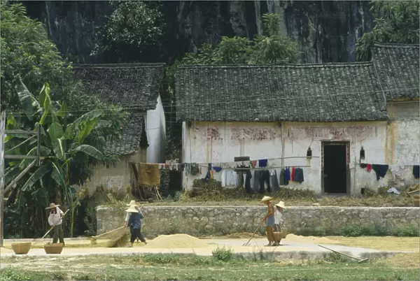10073205. CHINA Guangxi Province People drying grain outside a farmhouse