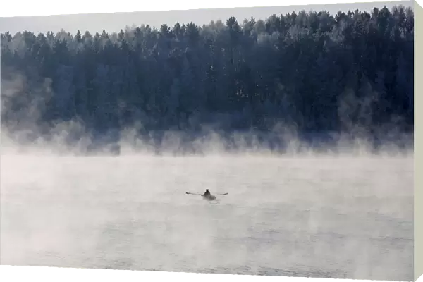 A man rows a boat through a frosty fog along the Yenisei River at air temperature