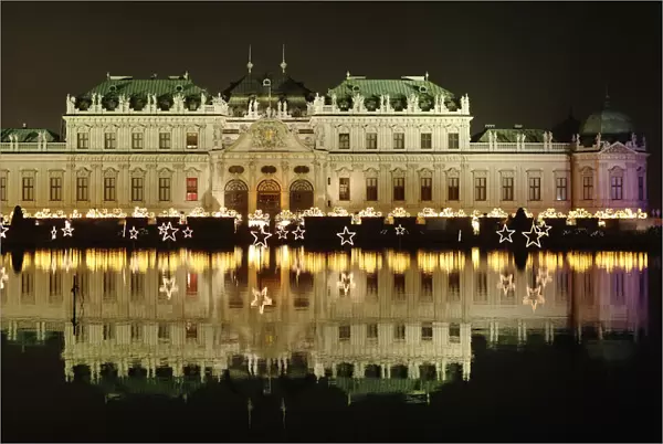 Belvedere palace is reflected in a pond behind the lights of an advent market in Vienna