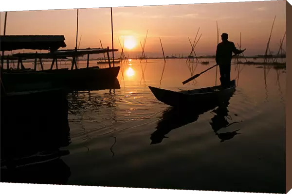 An Indonesian man rows fishing boat at sunset in central Java