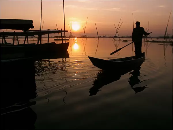 An Indonesian man rows fishing boat at sunset in central Java