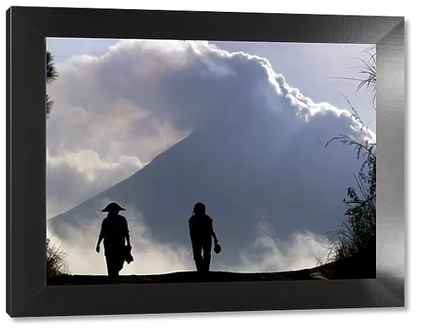 Indonesian farmers are silhouetted in front of Mount Merapi at Srumbung village, near