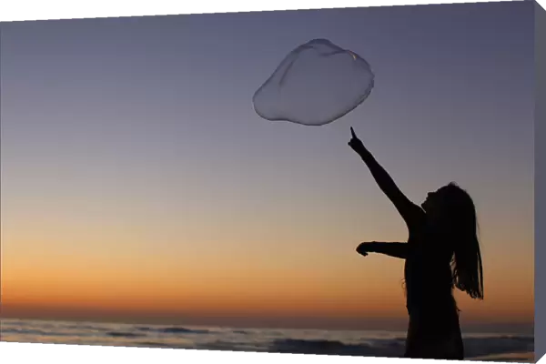 A girl plays with a giant bubble as the sun sets at Moonlight Beach in Encinitas