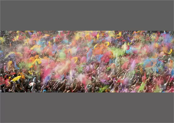 Crowd throwing bright colored powder paint in the air at Holi Fe