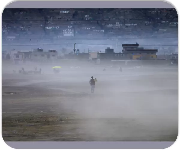 An Afghan man heads home walking through a dust cloud as the sun sets in Kabul