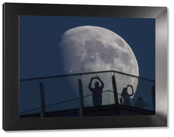 Visitors stand on the roof of a skyscraper as the moon rises over the skyline of Pudong