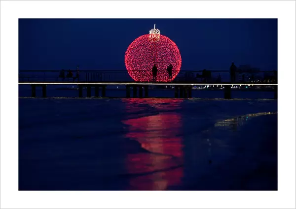 People are seen on a pier in front of a giant illuminated Christmas ball in Larnaca