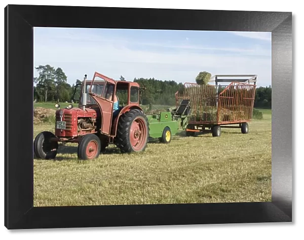 Tractor baling hay crop, baler tossing small bales into wagon, Sweden