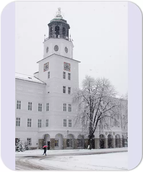 Europe, Austria, Salzburg. Person in snowstorm with red umbrella walking past white building