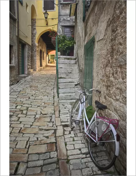 Bicycle and colorful cobblestone alleyway framed by arch, Rovigno, Croatia