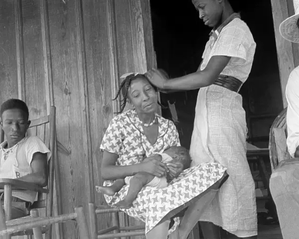 MIGRANT FAMILY, 1936. An African American woman braids another womans hair while