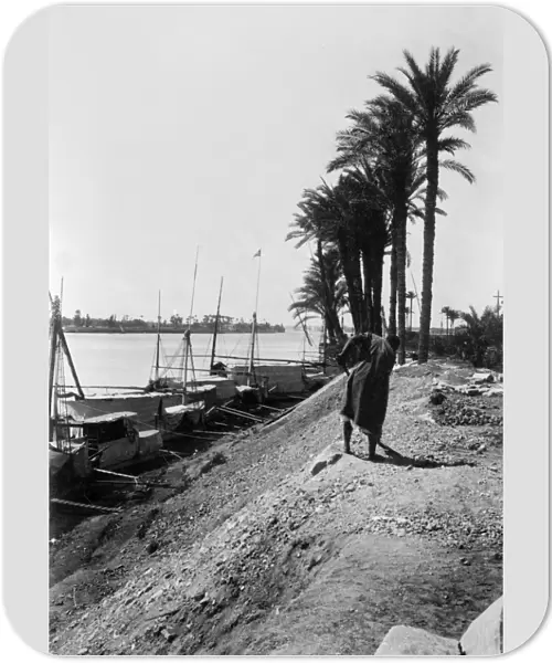 EGYPT: CAIRO. A view along the Nile with boats docked and a man shoveling on the shore
