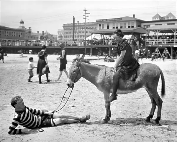ATLANTIC CITY: DONKEY. A young woman on the back of a donkey with a man, lying on the beach, holding the reins, Atlantic City, New Jersey. Photograph, c1901-1906