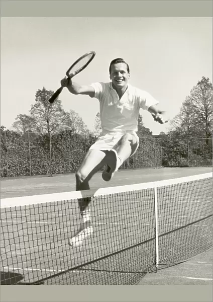 Man holding tennis racquet leaping over tennis net, 1950-60s, black and white