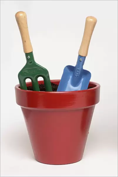 Red flowerpot with garden fork and trowel planted in it