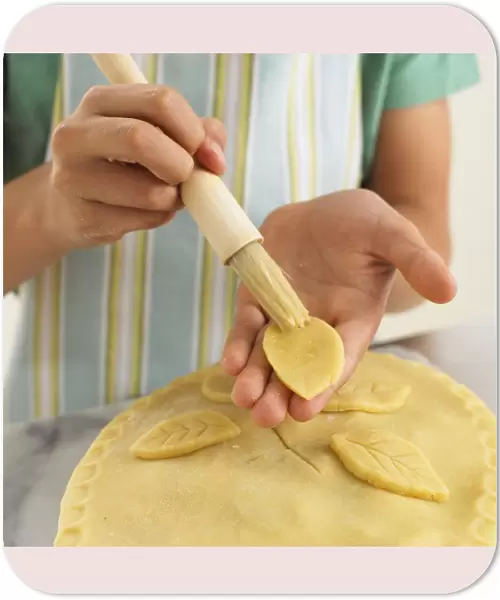 Girl brushing pie crust decoration with egg, close-up