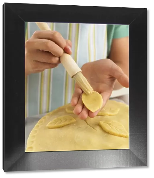 Girl brushing pie crust decoration with egg, close-up