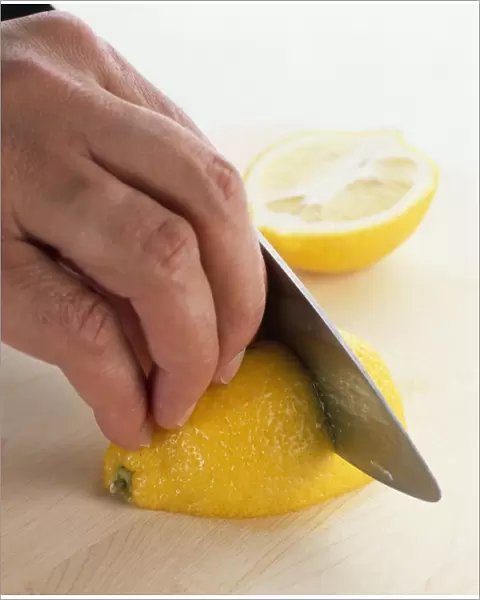 Hand shown slicing a lemon with a sharp knife, close-up