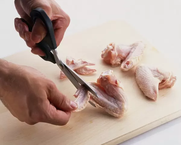 Using scissors to remove wings tips from chicken on wooden chopping board, close-up