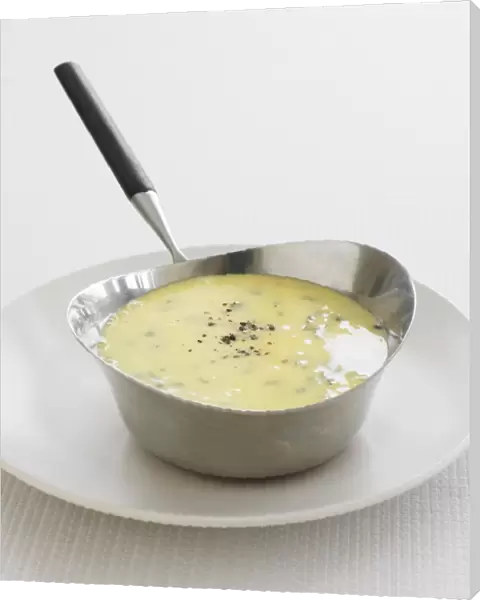 Bearnaise sauce, flavoured with tarragon and black pepper, in saucepan, on plate, close-up