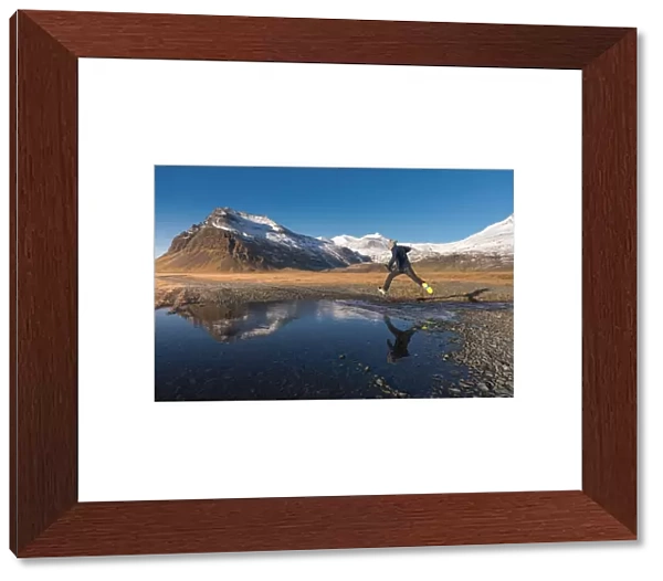 a man jumping across a water with snow mountain background