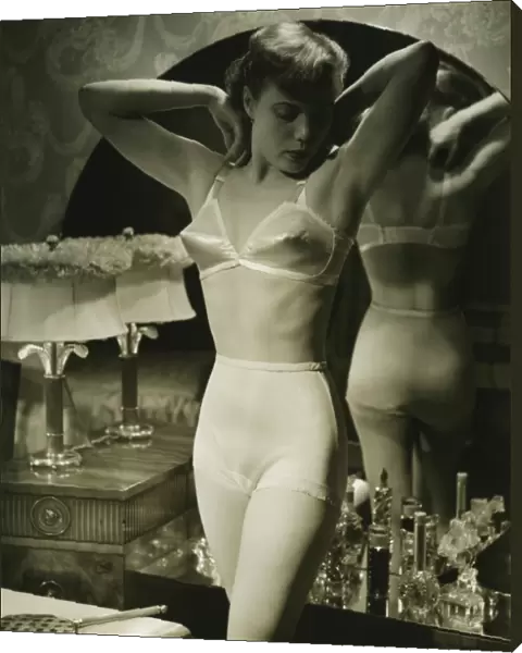 Young woman in underwear standing by mirror, (B&W)
