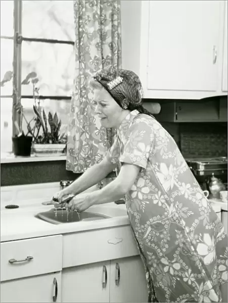 Housewife doing dishes at kitchen sink, (B&W)