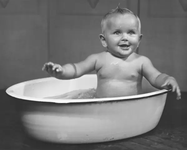 Baby boy (6-9 months) bathing in basin (B&W)