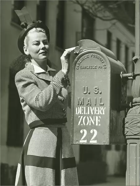Woman putting letter into mailbox, (B&W)