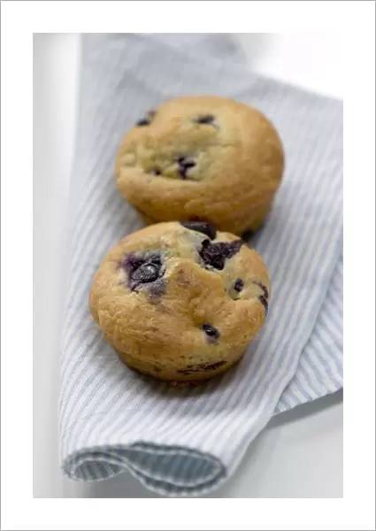 Freshly baked blueberry muffin on blue striped napkin with blue and white china credit